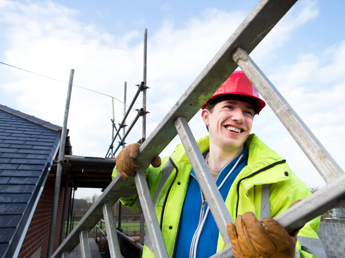 Roofer in hi-vis carrying a ladder on the scaffold