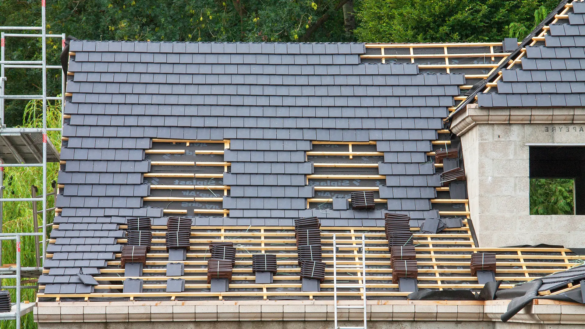 House on scaffolding part way through a re-roof with grey concrete tiles