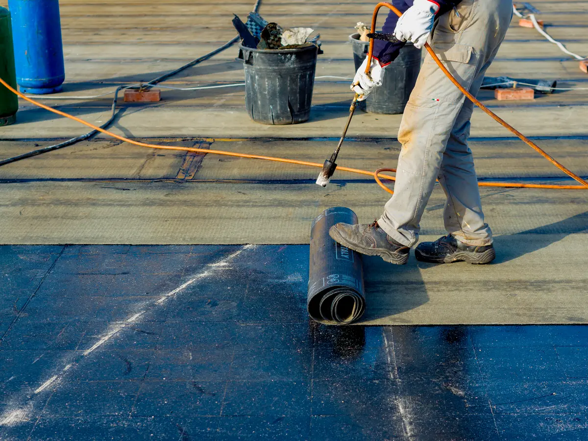 Roofer rolling out torch-on felt on a flat roof