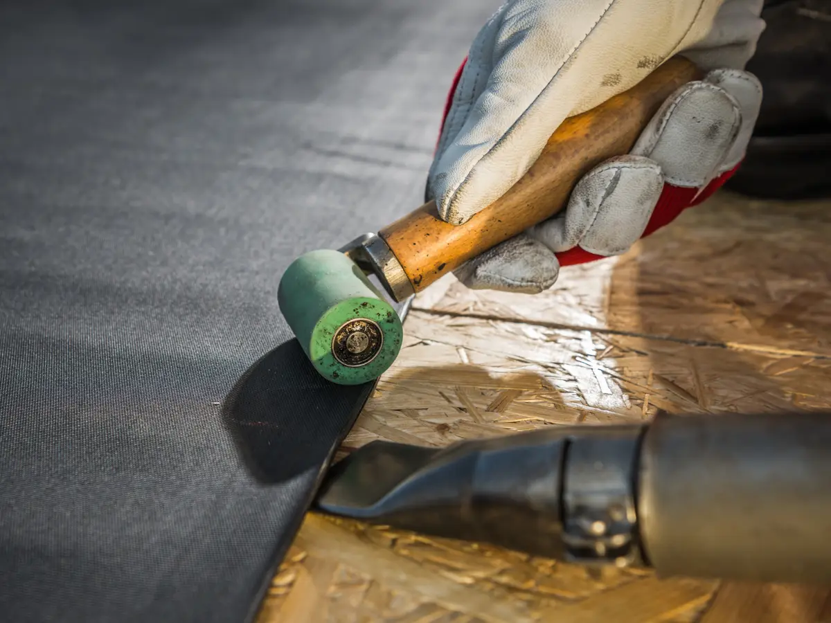 Roofer rolling down the seam of a black rubber membrane