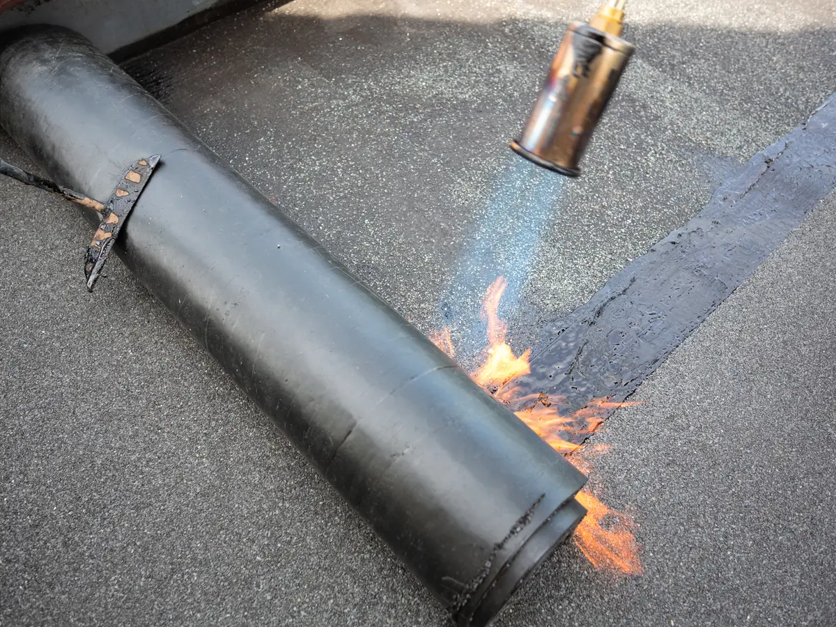Gas torch heating a roll of torch-on felt as it is laid