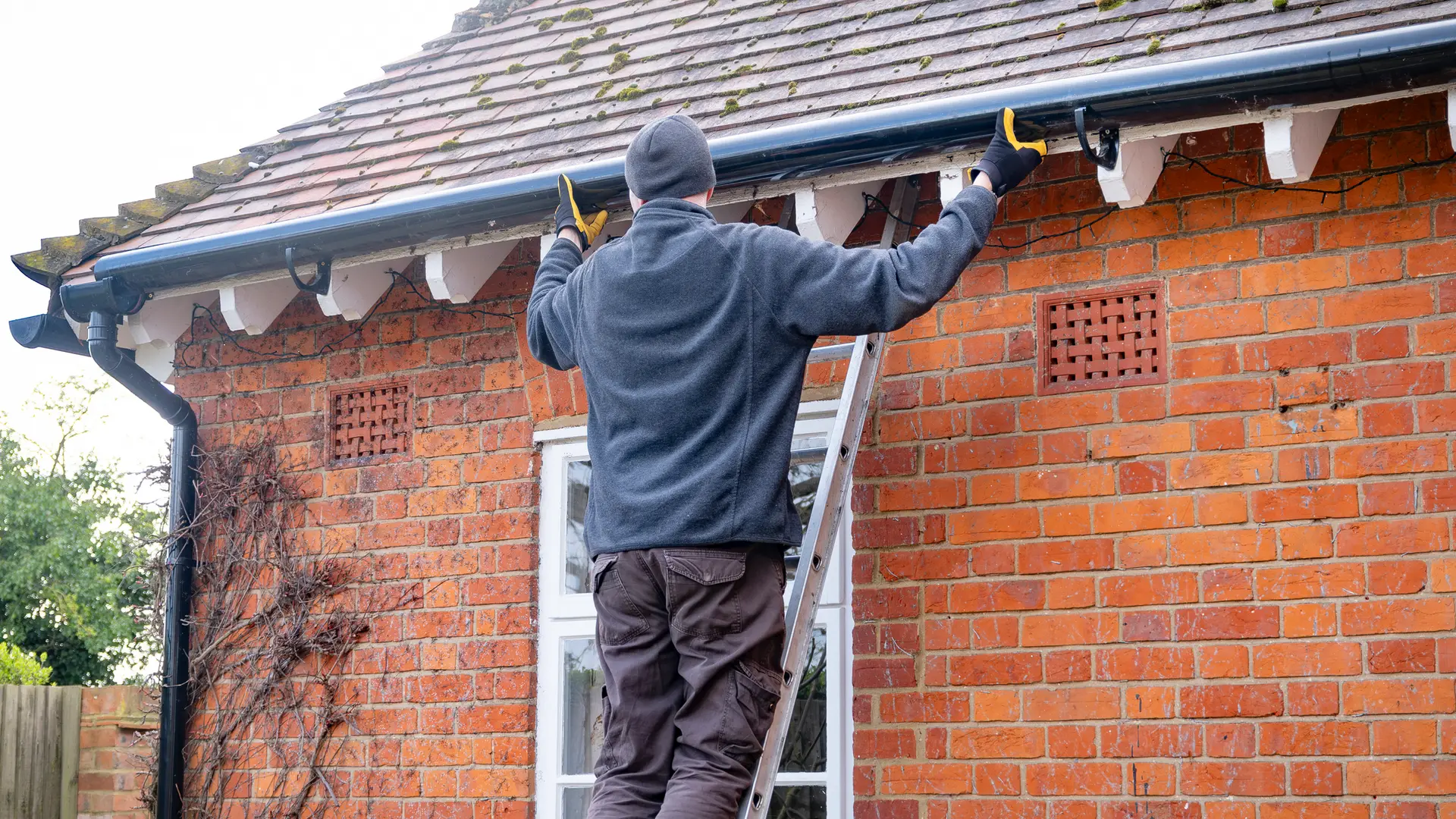 Gutter being cleared from a ladder on a red brick house